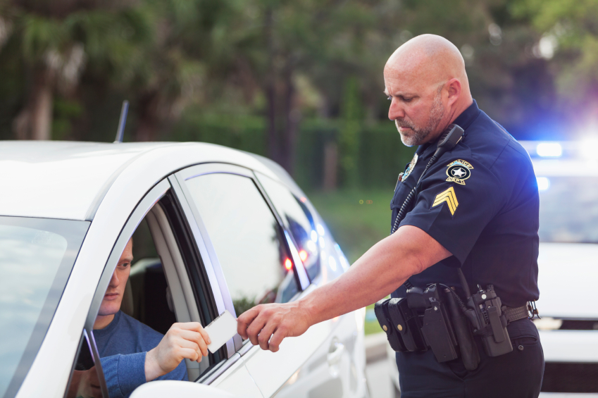 Policeman pulls over a driver for speeding.  Male driver is handing over his identification card.